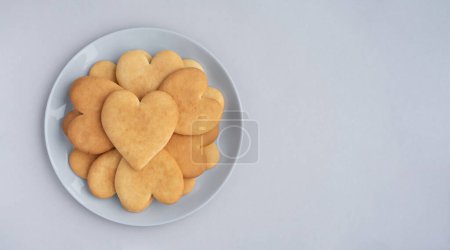 Téléchargez les photos : Assiette de délicieux biscuits en forme de cœur sur fond gris clair. Composition minimaliste pour la Saint-Valentin. Espace de copie, vue du dessus. - en image libre de droit