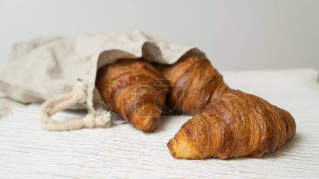 Croissants im Öko-Beutel auf einem Holztisch. Umweltfreundliche Leinentasche mit frischen Croissants.