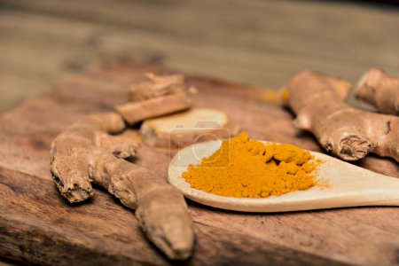 Photo for Close-up Turmeric curcumin powder in wooden spoon with fresh rhizome on wood background - Royalty Free Image