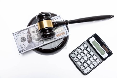 A legal gavel atop American currency with a calculator, depicting financial law or fines