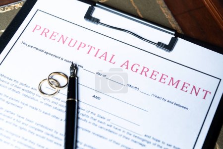 Close-up of a prenuptial agreement form with wedding rings and a fountain pen, indicating the legal aspects of marriage preparation