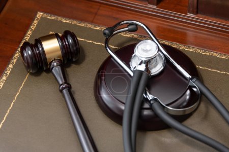 Un primer plano de un mazo de jueces y un estetoscopio negro encima de un libro legal, lo que significa la intersección de la ley y la medicina