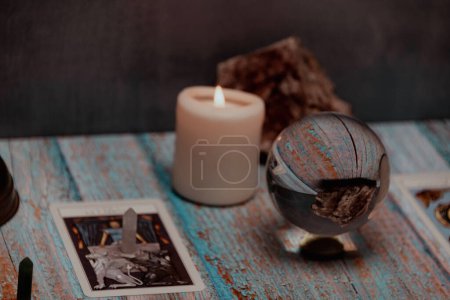 Lesung einer Tarotkarte mit Kerzen, Kristallen und mystischen Accessoires auf einem rustikalen Holztisch
