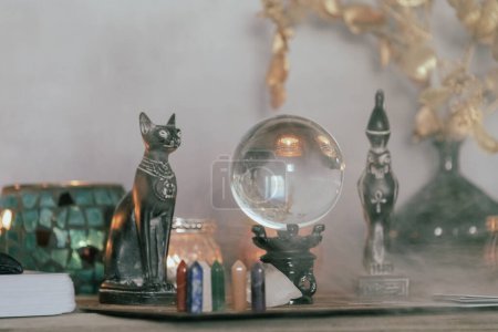 Eine stimmungsvolle Kulisse mit Kristallkugel, ägyptischen Katzenstatuen, Kerzen und Kristallen, die ein mystisches Ambiente schaffen