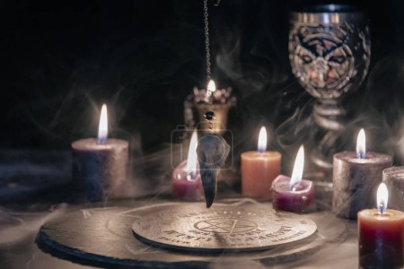 Téléchargez les photos : Une étrange configuration rituelle occulte avec des bougies allumées, un symbole mystique sur ardoise et un gobelet cérémonial dans un décor sombre et lunatique - en image libre de droit