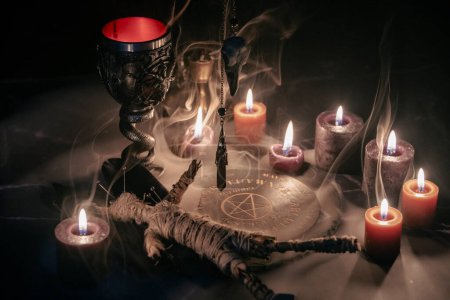 Photo for A haunting occult setup featuring a pendulum, mystical symbols, candles, a voodoo doll, and a ritual goblet amidst swirling smoke - Royalty Free Image