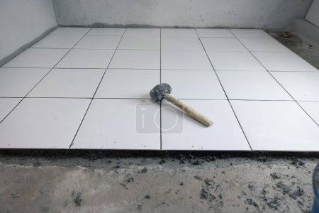 Photo for Tile floor under construction at interior. Include mallet tool, concrete mortar cement and white square ceramic tile. Finishing material for decor surface in bathroom, kitchen and shower room. - Royalty Free Image