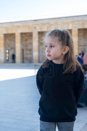 Photo for A blond little girl wearing a black sweetshirt is visiting the mausoleum in Ankara. The little girl is sad and grieving for Atatrk. Selective Focus Girls Face. - Royalty Free Image