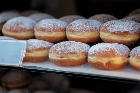 Foto de Berliner Pfannkuchen, a German donut, traditional yeast dough deep fried filled with chocolate cream or strawberry marmalade  and sprinkled with powdered sugar in showcase. Selective Focus. - Imagen libre de derechos