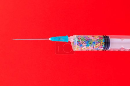 Photo for A classic disposable syringe filled with symbolic hearts. Love concept. Background with copy space for text. Red backdrop. - Royalty Free Image