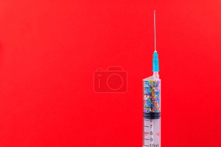 Téléchargez les photos : A classic disposable syringe filled with symbolic hearts. Love concept. Background with copy space for text. Red backdrop. - en image libre de droit