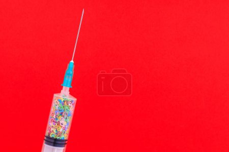 Téléchargez les photos : A classic disposable syringe filled with symbolic hearts. Love concept. Background with copy space for text. Red backdrop. - en image libre de droit