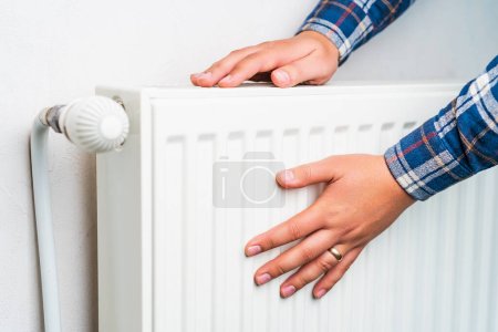 Foto de Hands on the radiator of the heating system, selective focus. Background with copy space - Imagen libre de derechos