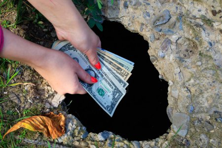 Photo for The hand drops dollars into a black hole in concrete. Abstract concept of waste of money. - Royalty Free Image