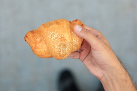 Guy's hand holds a croissant, snack and fast food concept. Selective focus on hands with blurred background and copy space for text.