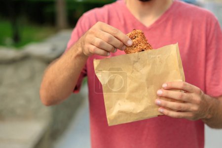 In der Hand hält ein Mann ein süßes Gebäck mit Marmelade, Snacks und Fast Food. Selektiver Fokus auf Hände mit verschwommenem Hintergrund und Kopierraum für Text.
