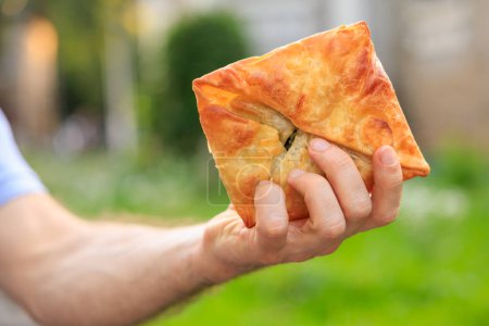 A man's hand holds a puff pastry with cheese, snack and fast food concept. Selective focus on hands with blurred background and copy space for text.