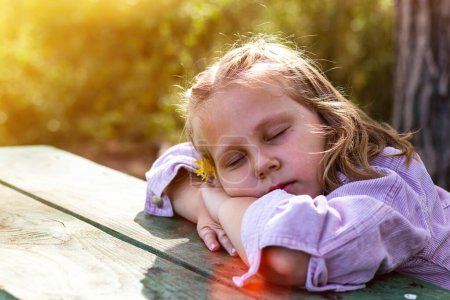 Téléchargez les photos : La petite fille se repose dans le parc. Espace de copie. Bébé heureux dort en marchant à l'extérieur. - en image libre de droit