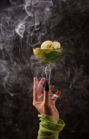 Téléchargez les photos : Cocktail aux pommes vert Halloween avec main de sorcière, fond sombre - en image libre de droit