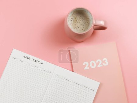 Téléchargez les photos : Top view or flat lay of habit tracker book on pink diary or planner 2023 and pink cup of coffee on pink background with copy space. - en image libre de droit