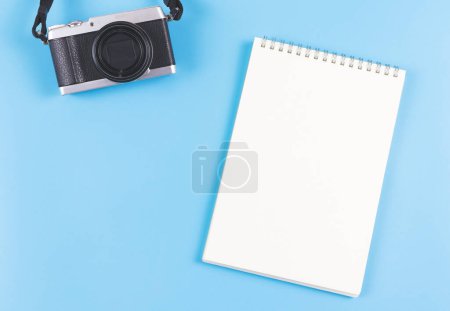 Foto de Vista superior o disposición plana de la página en blanco abrió el cuaderno y la cámara en el fondo azul. - Imagen libre de derechos