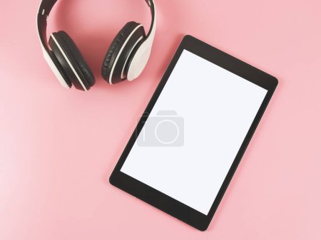 Top view or flat lay of tablet with white blank screen and headphones on pink background.
