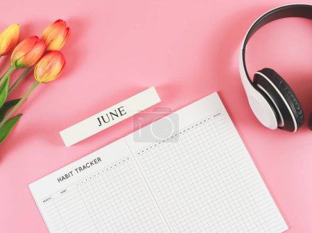 Photo for Top view or flat lay of habit tracker book with wooden calendar June,  headphones and tulips  on pink background. - Royalty Free Image