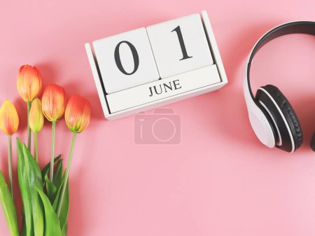 Photo for Top view or flat lay of wooden calendar with date June 01, headphones and  orange  yellow tulips on pink background, copy space. - Royalty Free Image