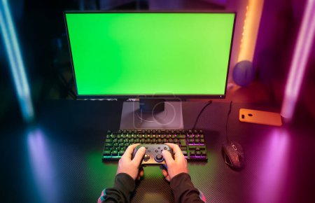 POV of gamer hands playing with joystick on green screen computer in trendy and stylish room with neon light. Streaming video games concept. High quality photo