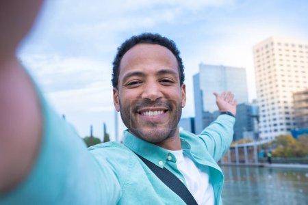 Téléchargez les photos : Jeune Afro-Américain prenant un selfie souriant heureux de montrer la nouvelle ville où il vit. Touriste voyage autour du monde concept. Photo de haute qualité - en image libre de droit