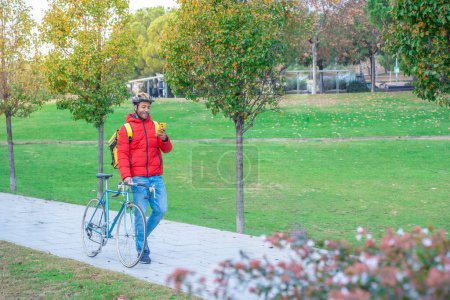 Foto de Concepto de entrega de alimentos. Joven conductor afroamericano sonriente con mochila y bicicleta con aspecto de teléfono inteligente en la ciudad para entregar productos para los clientes que ordenan compras en línea. Foto de alta calidad - Imagen libre de derechos