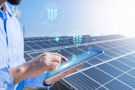 Foto de Unrecognizable engineer with a tablet with eco holograms with photovoltaic solar panel system plant in the background. Green clean energy concept. - Imagen libre de derechos