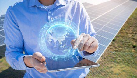 Foto de Unrecognizable engineer with a tablet with earth HUD hologram with photovoltaic solar panels system plant in the background. Green clean alternative energy concept. - Imagen libre de derechos