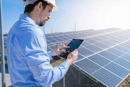 Foto de Ingeniero que trabaja con una tableta con la planta del sistema del panel solar fotovoltaico en el fondo. Concepto de energía limpia verde. - Imagen libre de derechos