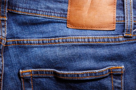 Photo for Worn denim trousers with leather blank label. Machine stitch close up. Denim texture in blue. The concept of repairing old clothes. Sewing factory. Fashionable aging clothes. - Royalty Free Image