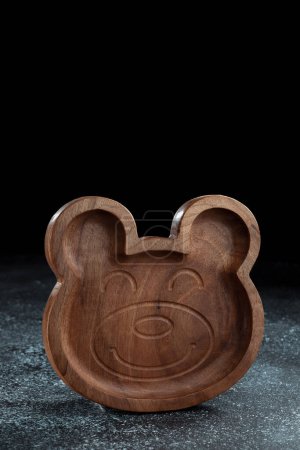 Photo for A plate for children in the shape of a bear is made of wood for serving snacks, fruits, nuts, cheeses, meat and original serving of main dishes. Accessories for a modern kitchen. - Royalty Free Image
