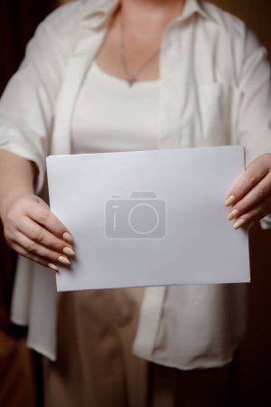 Photo for Creative start: a blank piece of paper waiting for inspiration. White sheet of paper in female hands. Place for an inscription on a psychological theme. White sheet of paper in female hands. - Royalty Free Image