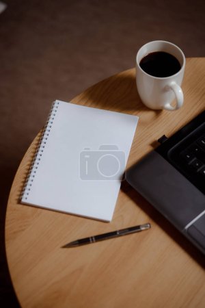Schreibtischhoch: Laptop, leere Seite und aromatischer Kaffee. Kaffee kreativ: Ideen auf einem weißen Blatt mit einem Kaffeegetränk. Business in allen Schattierungen: Professionelle Eleganz in jedem Rahmen.