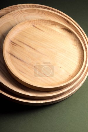 Plaques plates en bois sur fond vert foncé. Le concept de vaisselle écologique. Produits pour cuisine moderne. Harmonie naturelle : assiettes en bois dans une cuisine écologique. Nuances de lampe chaudes.