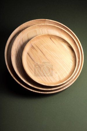 Plaques plates en bois sur fond vert foncé. Le concept de vaisselle écologique. Produits pour cuisine moderne. Harmonie naturelle : assiettes en bois dans une cuisine écologique. Nuances de lampe chaudes.