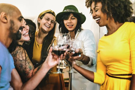 Téléchargez les photos : Cheerful group of multiethnic best friends celebrating aperitif drinking and toasting with red wine standing indoors - multiracial best friends have fun cheering at home party --food and people lifestyle concept - en image libre de droit
