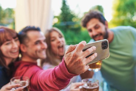 Photo for Happy friends at terrace party taking selfie with their smartphone having fun together - millennials young people taking memories outdoors in the terrace - blurred faces focus on the phone - Royalty Free Image