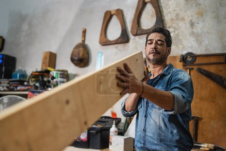 Téléchargez les photos : A carpenter visually checks a plank of wood in his vintage shop - Concept of woodworking, small business, ancient crafts and small craftsmen - en image libre de droit