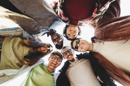 Foto de Multiethnic group of young friends joining heads in circle watching down to the camera - international youth culture concept with different people enjoining life together - people lifestyle concept - Imagen libre de derechos