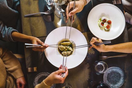 Groupe de personnes partageant des boulettes chinoises à la vapeur - vue zénithale de la table avec quatre mains tenant des baguettes sur la fusion restaurant de luxe alimentaire - personnes, concept de nourriture et de boisson - style de vie photographie alimentaire