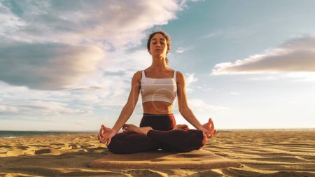Junge Frau praktiziert Yoga, macht Padmasana-Übungen, meditiert in Lotus-Pose mit Mudra-Geste, trainiert mit Top und Leggings in der Natur - Achtsamkeit und Fernweh Lifestylekonzept