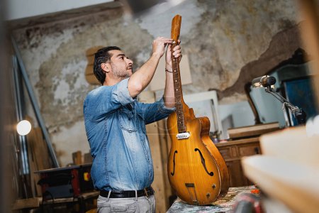 Téléchargez les photos : Luthier craftsman fixing a guitar screwing the truss rod in his vintage studio-garage - music, art, crafts and people lifestyle concept - en image libre de droit