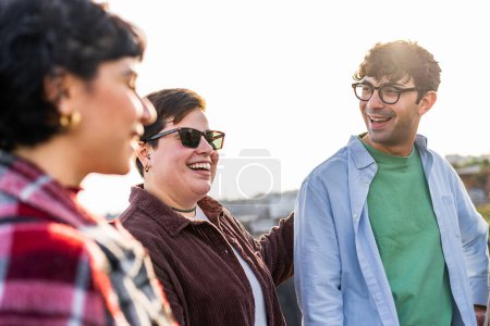 Best friends talking carefree laughing outdoors - group of young people smiling and having fun bonding together - a man and two women millennials generation lifestyle concept