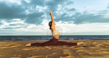 Attractive young Caucasian women practicing monkey pose relaxing on the beach. Hanumanasana. - calm and meditation - people lifestyle concept