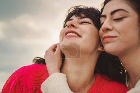 Foto de A close-up shot of two Caucasian women showing affection and love by embracing each other tightly, one of them with a nose piercing. The photo was taken outdoor in natural light - Imagen libre de derechos